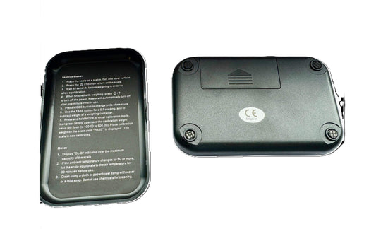 Achterzijde van een digitale pocketweegschaal met batterijcompartiment en antislipvoetjes, naast het deksel met gebruiksinstructies en kalibratiehandleiding in het Engels.